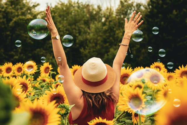 happy lady wearing a sun hat in a field of sunflowers - she's health because she's invested in FlexTerm from Everest